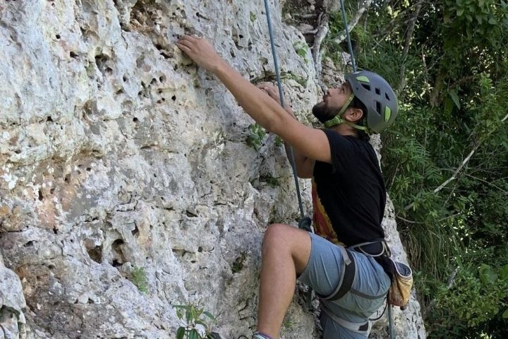Person rock climbing with a helmet, secured by ropes, on a rocky surface.