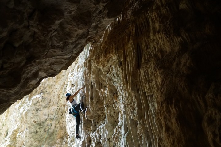 Person rock climbing on textured cave wall under subdued lighting.